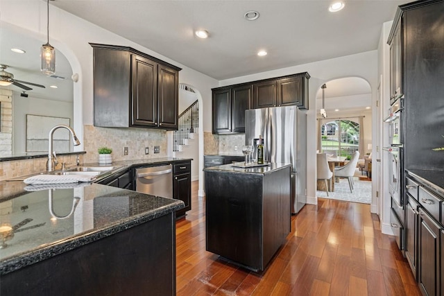 10709 Pointe View Dr, Austin, TX 78738 - kitchen featuring arched walkways, appliances with stainless steel finishes, a ceiling fan, dark stone countertops, and dark brown cabinetry