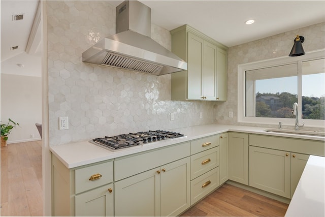 kitchen featuring stainless steel gas stovetop, sink, backsplash, wall chimney exhaust hood, and light hardwood / wood-style flooring