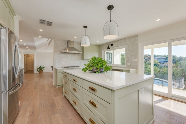 kitchen featuring stainless steel refrigerator with ice dispenser, light wood-type flooring, a kitchen island, pendant lighting, and wall chimney range hood