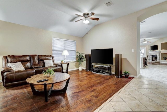 living room with light tile patterned flooring, lofted ceiling, ceiling fan, and a brick fireplace