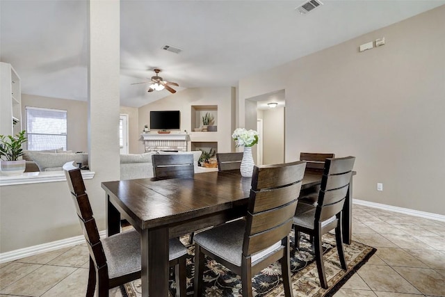 dining room featuring lofted ceiling, a fireplace, ceiling fan, and light tile patterned flooring