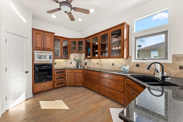 kitchen with sink, light hardwood / wood-style flooring, dark stone countertops, stainless steel microwave, and black oven