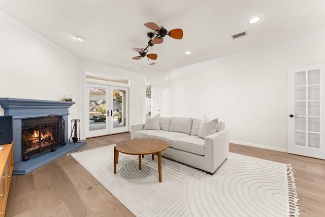 living room with ornamental molding, french doors, ceiling fan, and light wood-type flooring