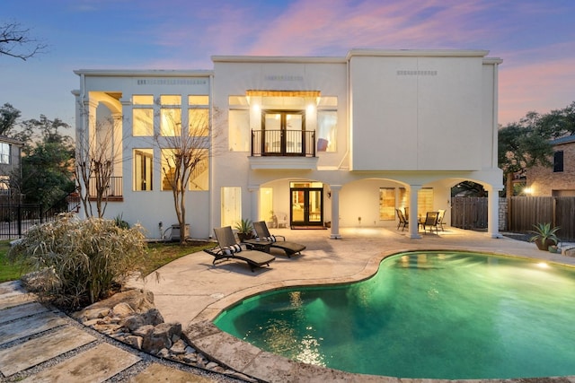 back house at dusk with a fenced in pool, a balcony, and a patio area