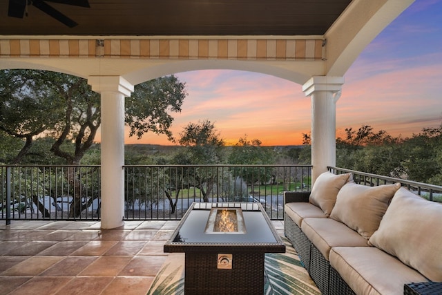 patio terrace at dusk with an outdoor living space with a fire pit, ceiling fan, and a water view