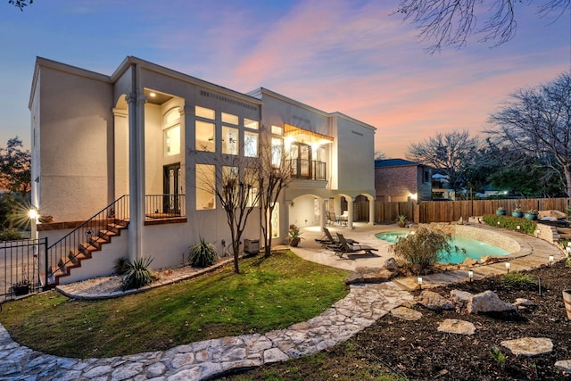 back house at dusk featuring a balcony, a fenced in pool, and a patio