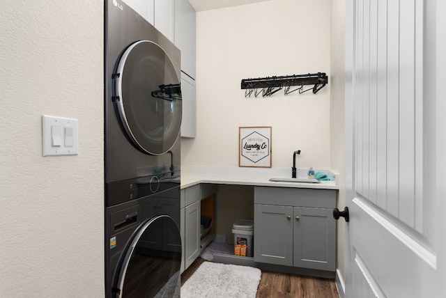 clothes washing area featuring cabinets, stacked washer and dryer, dark hardwood / wood-style floors, and sink