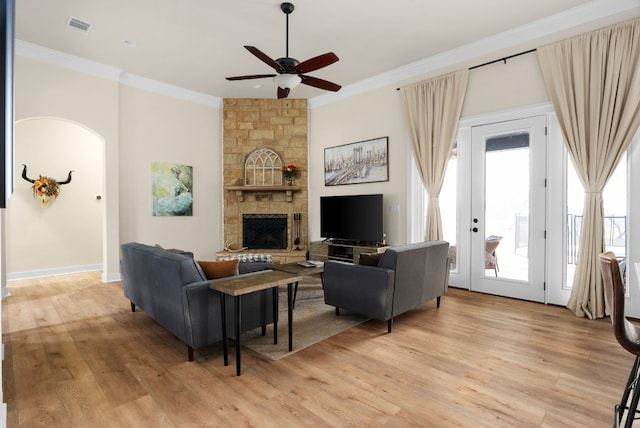 living room featuring ceiling fan, ornamental molding, a stone fireplace, and light hardwood / wood-style flooring