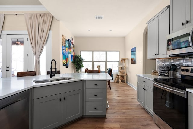 kitchen featuring sink, gray cabinetry, light hardwood / wood-style floors, kitchen peninsula, and stainless steel appliances