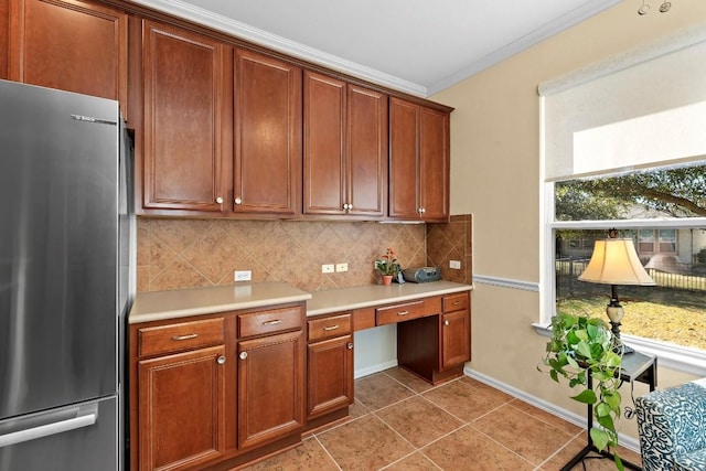 kitchen featuring built in desk, light tile patterned floors, stainless steel refrigerator, ornamental molding, and decorative backsplash