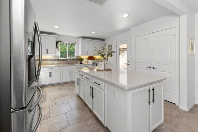 kitchen featuring sink, light stone counters, stainless steel fridge with ice dispenser, a kitchen island, and white cabinets