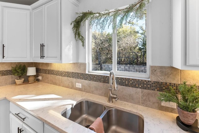 kitchen with white cabinetry, sink, light stone counters, and tasteful backsplash