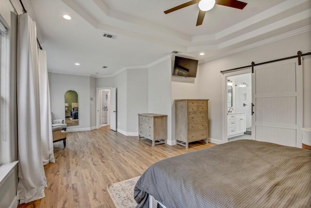 bedroom with a barn door, ornamental molding, a tray ceiling, and light hardwood / wood-style flooring