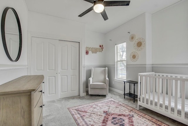 bedroom with a crib, light colored carpet, a closet, and ceiling fan