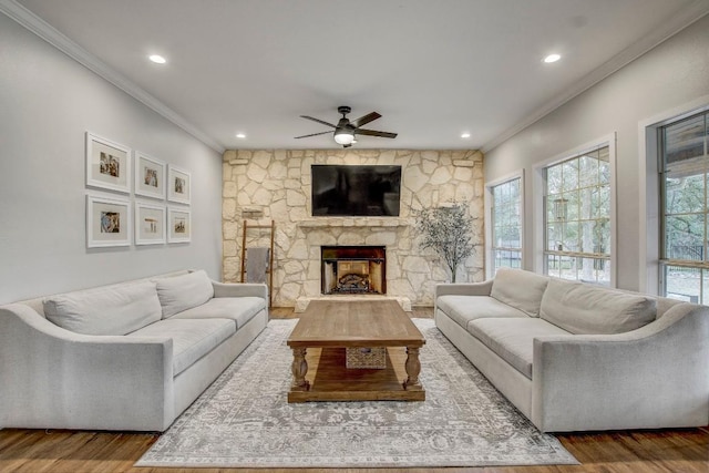 living room with crown molding, ceiling fan, a stone fireplace, and hardwood / wood-style flooring