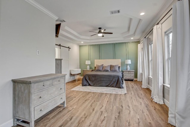 bedroom featuring ornamental molding, a tray ceiling, a barn door, and light hardwood / wood-style flooring