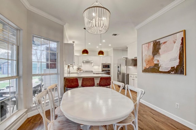 dining room featuring a healthy amount of sunlight, ornamental molding, and light wood-type flooring