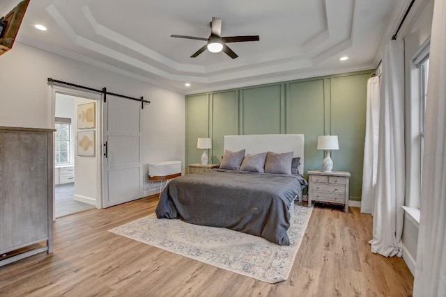 bedroom with a raised ceiling, a barn door, and light hardwood / wood-style floors