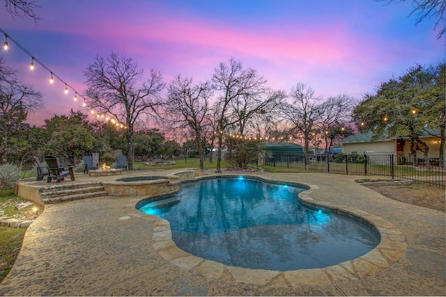 pool at dusk featuring a patio and an in ground hot tub