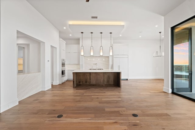 kitchen with sink, backsplash, paneled built in fridge, white cabinets, and a large island with sink