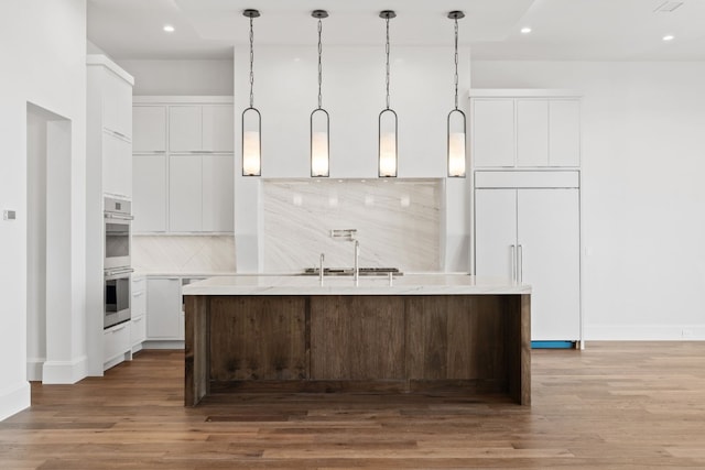 kitchen featuring white cabinetry, double oven, paneled fridge, and a center island with sink