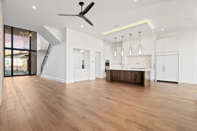 unfurnished living room featuring ceiling fan, sink, light wood-type flooring, and a wall of windows