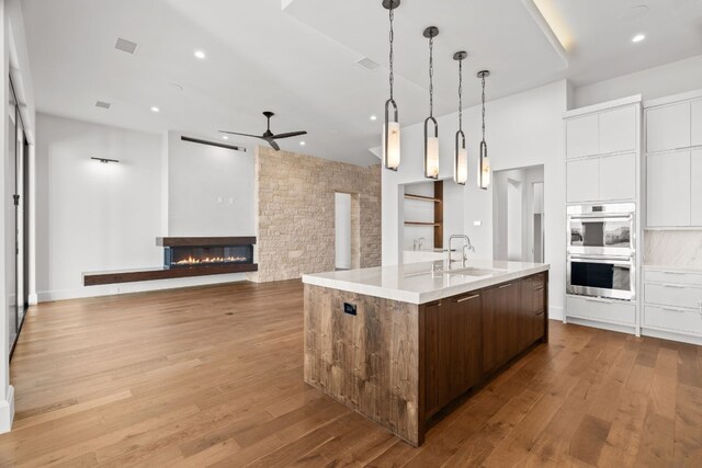 1409 Apache Tears, Horseshoe Bay, TX 78657 - kitchen featuring stainless steel double oven, a ceiling fan, modern cabinets, white cabinets, and a glass covered fireplace