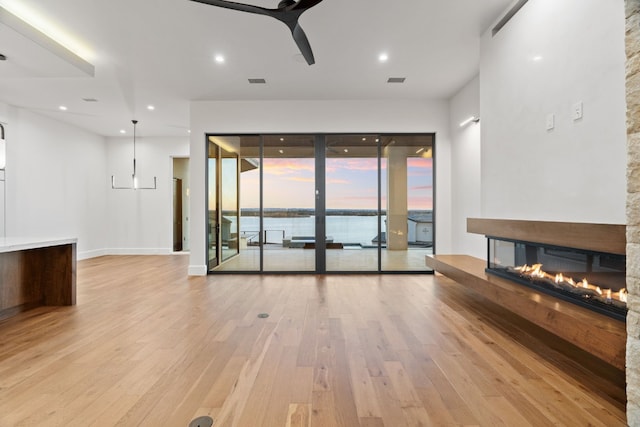 unfurnished living room with ceiling fan, a stone fireplace, and light hardwood / wood-style floors