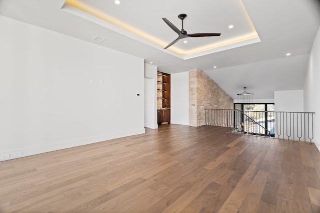 interior space featuring a raised ceiling, ceiling fan, and light hardwood / wood-style flooring