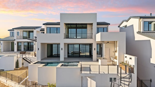 back house at dusk featuring a swimming pool with hot tub and a patio