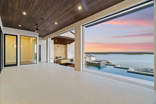 patio terrace at dusk with a water view, ceiling fan, and a pool with hot tub