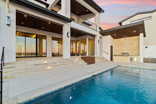 back house at dusk featuring ceiling fan, exterior kitchen, a balcony, and a patio area