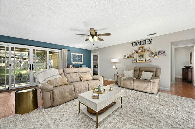 living room featuring ceiling fan, light hardwood / wood-style flooring, and a textured ceiling