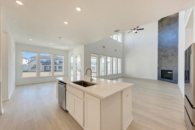 kitchen with sink, a kitchen island with sink, a fireplace, white cabinets, and stainless steel dishwasher