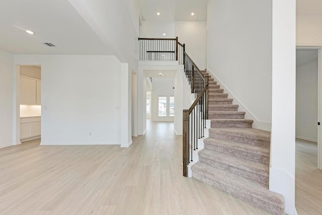 foyer entrance with visible vents, wood finished floors, stairway, baseboards, and a towering ceiling