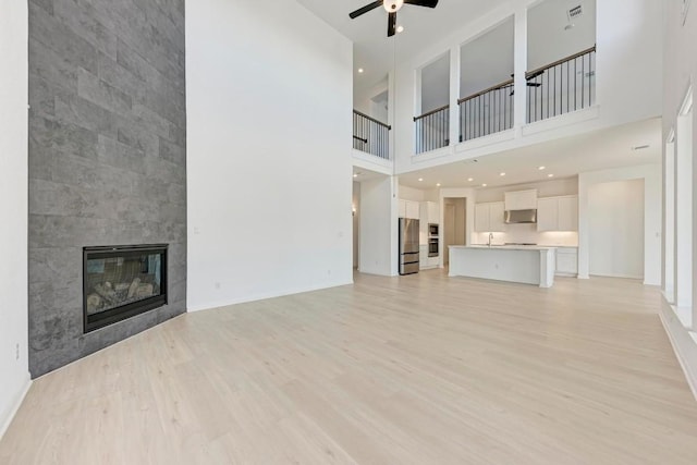 unfurnished living room featuring ceiling fan, sink, a fireplace, and light hardwood / wood-style flooring