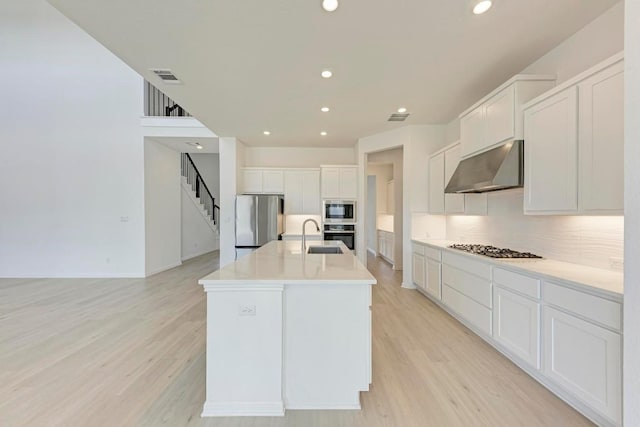 kitchen featuring appliances with stainless steel finishes, tasteful backsplash, light hardwood / wood-style floors, white cabinets, and a center island with sink