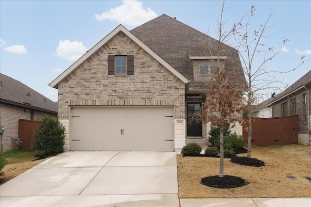 view of front facade featuring a shingled roof, brick siding, driveway, and fence