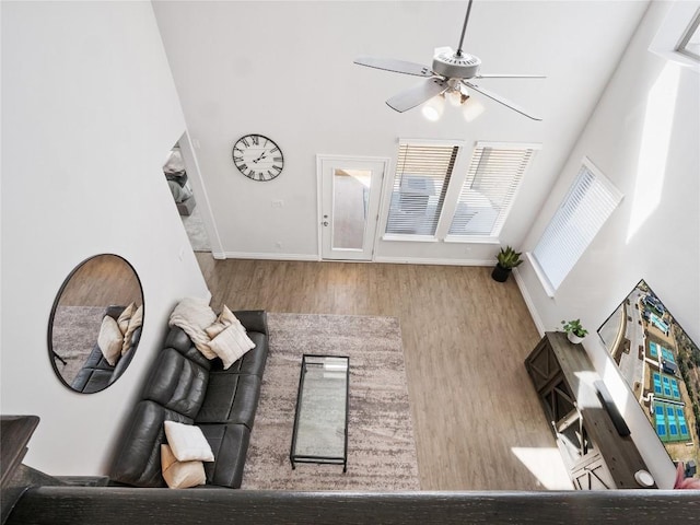 living room with baseboards, wood finished floors, a towering ceiling, and a ceiling fan