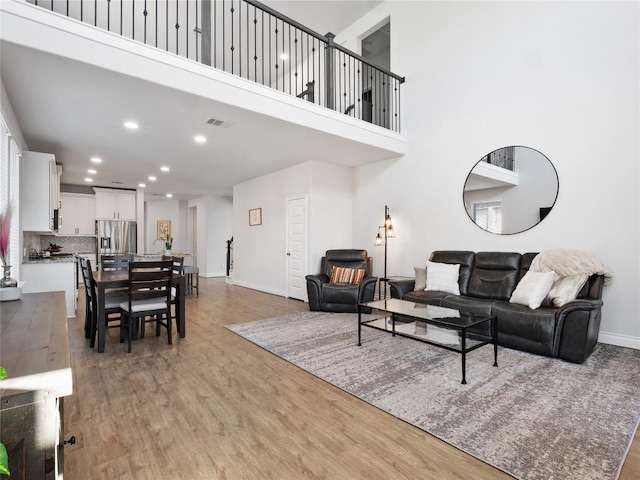 living area featuring recessed lighting, visible vents, light wood-style flooring, a high ceiling, and baseboards