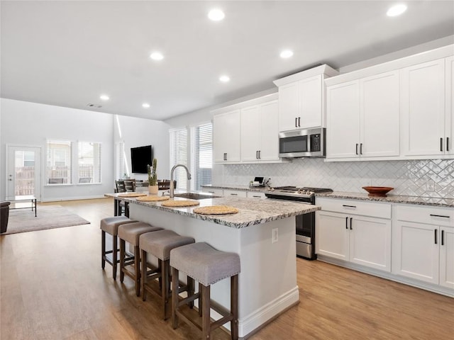 kitchen featuring an island with sink, light stone counters, open floor plan, stainless steel appliances, and a sink