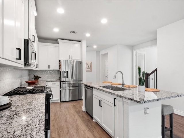 kitchen featuring visible vents, appliances with stainless steel finishes, white cabinets, a sink, and wood finished floors