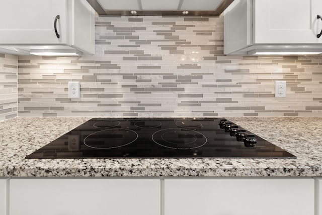 kitchen featuring tasteful backsplash, black electric stovetop, white cabinets, and light stone counters