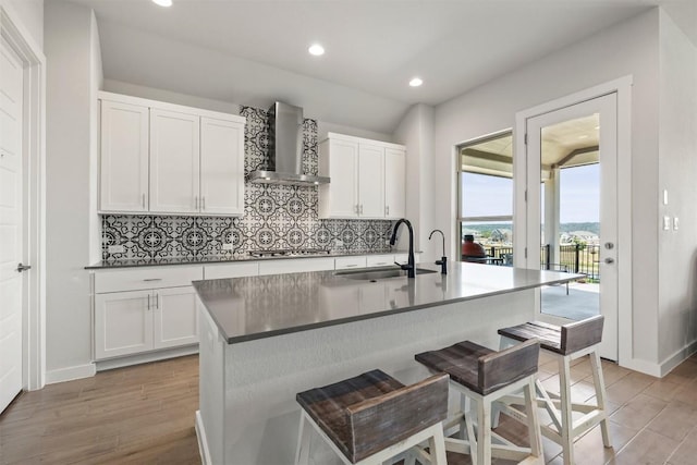 kitchen featuring sink, white cabinets, wall chimney exhaust hood, and a breakfast bar