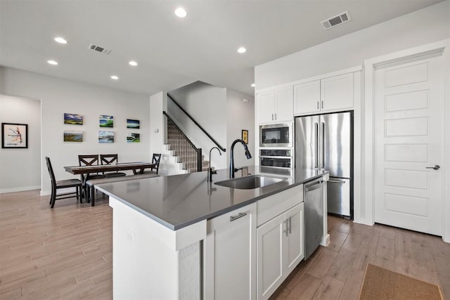 kitchen featuring an island with sink, sink, white cabinets, stainless steel appliances, and light hardwood / wood-style flooring