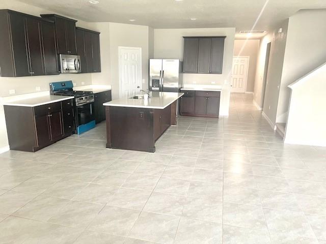 kitchen featuring dark brown cabinetry, sink, light tile patterned floors, an island with sink, and stainless steel appliances