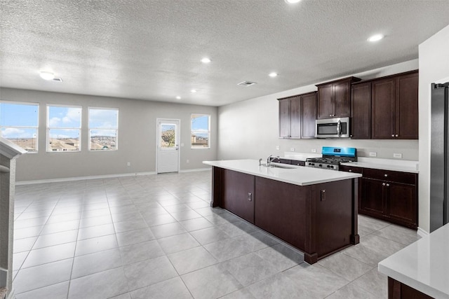 kitchen with sink, light tile patterned floors, stainless steel appliances, dark brown cabinetry, and a center island with sink