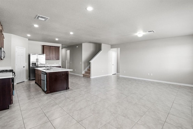 kitchen featuring dark brown cabinetry, sink, a center island with sink, a textured ceiling, and stainless steel appliances