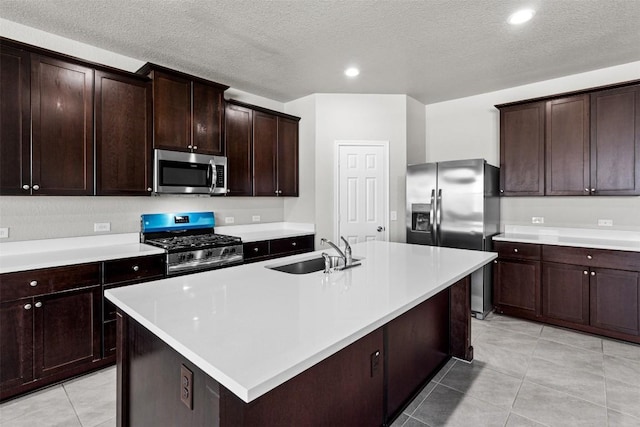 kitchen featuring sink, light tile patterned floors, a kitchen island with sink, stainless steel appliances, and dark brown cabinetry