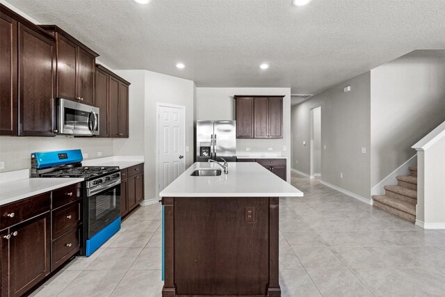 kitchen featuring dark brown cabinetry, sink, a center island with sink, a textured ceiling, and stainless steel appliances